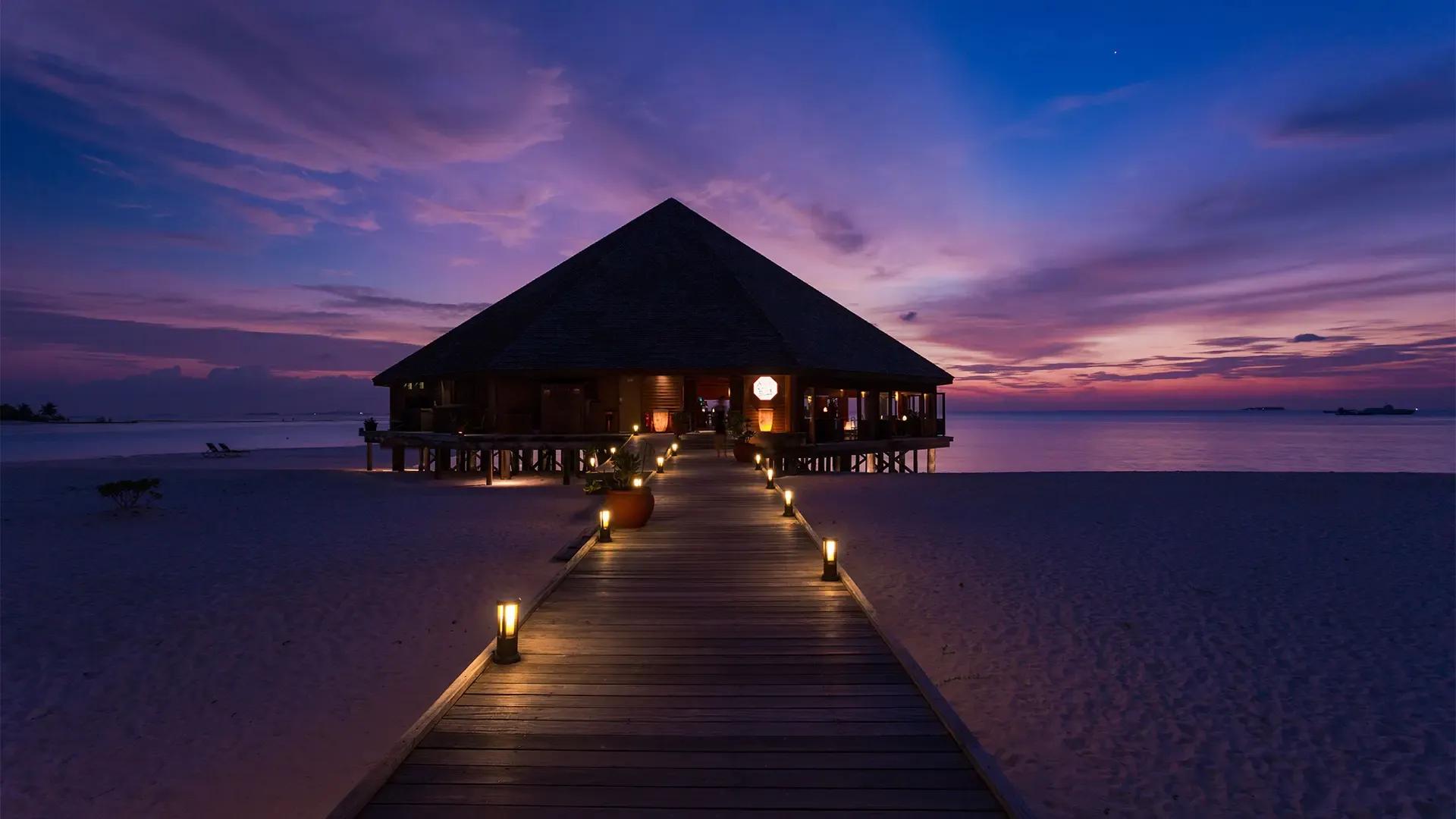Пирс с фонарями, ведущий к ресторану на воде в сумерках, Meeru Island Resort & Spa