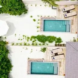 Beach Pool Villa сверху: два бассейна на песке, зонт и зелёная изгородь между виллами