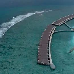 Water Villa с воздуха: изогнутый пирс над рифом и виллы на сваях у кромки лагуны