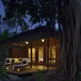 Beach Villa на Курамати вечером: свет из окон и корни баньяна у террасы