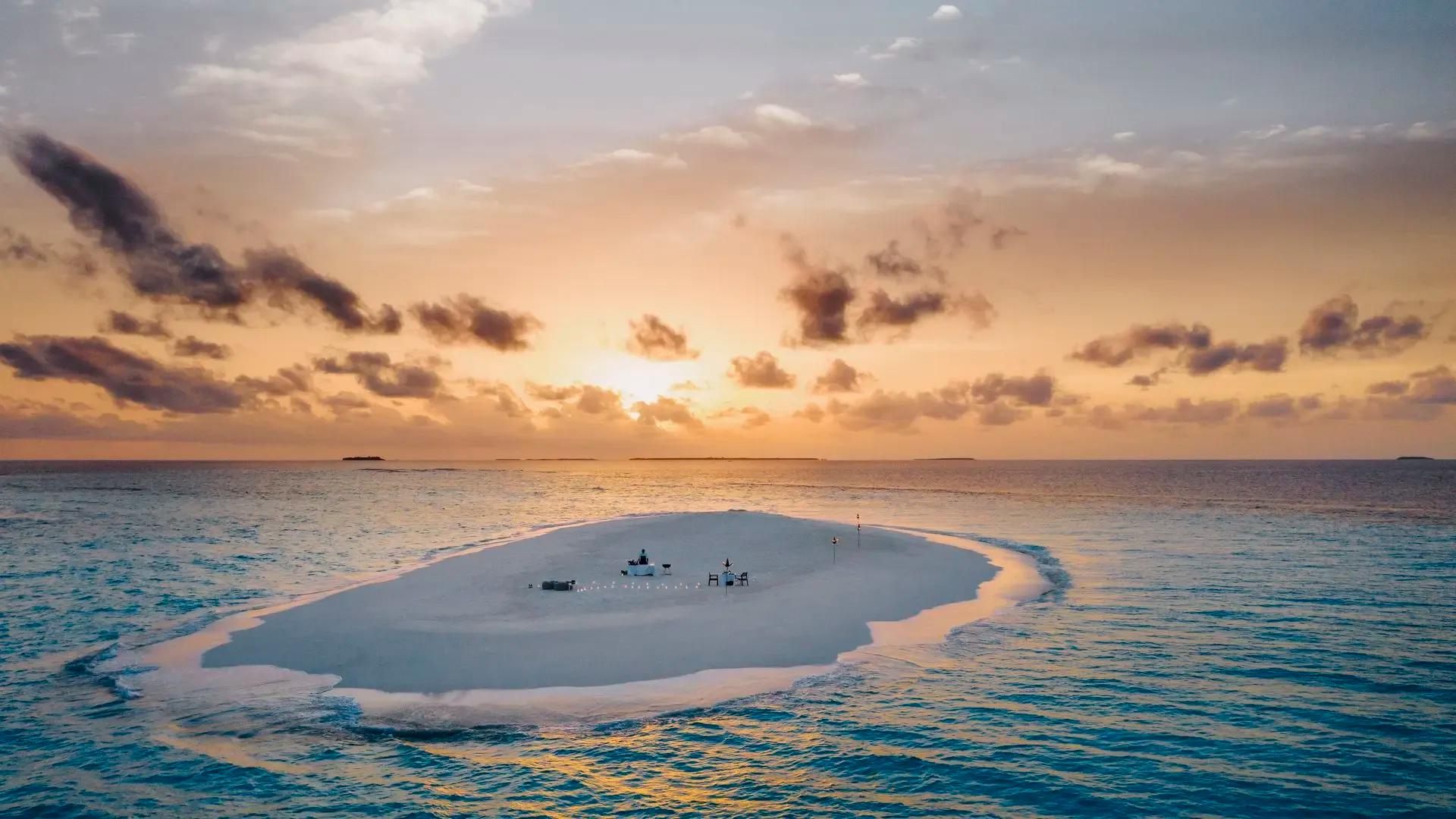 Стол для ужина на песчаной косе One&Only Reethi Rah на закате, вокруг лагуна, атолл Каафу