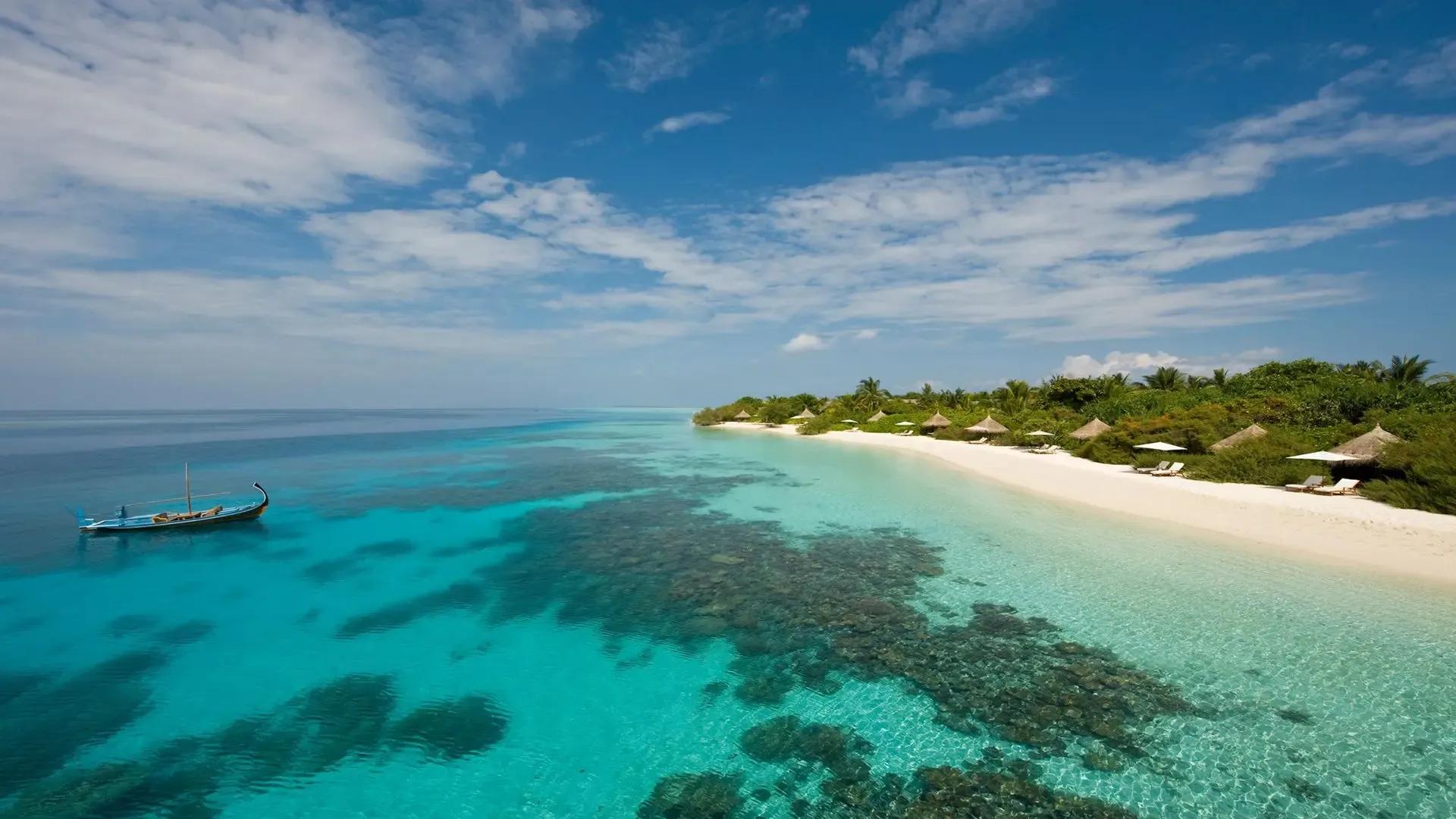 Белый пляж, бирюзовая лагуна и лодка дони у берега Four Seasons Landaa Giraavaru